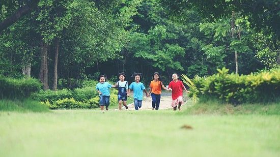 A group of children running on a grass field with trees in the background, parallel to each other.